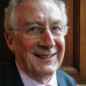 Elderly man with glasses smiling broadly, wearing a suit and tie.